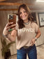 Woman taking a mirror selfie wearing a beige sweater with 'HOWDY' text.